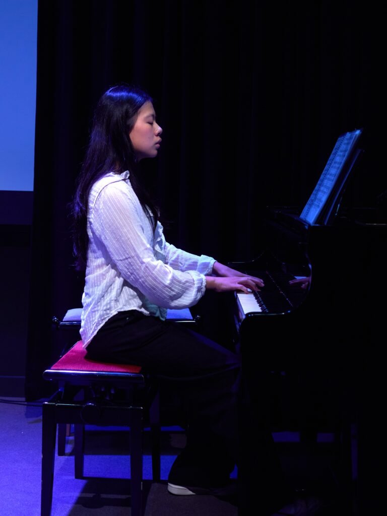 Jove dona tocant el piano en un escenari fosc.