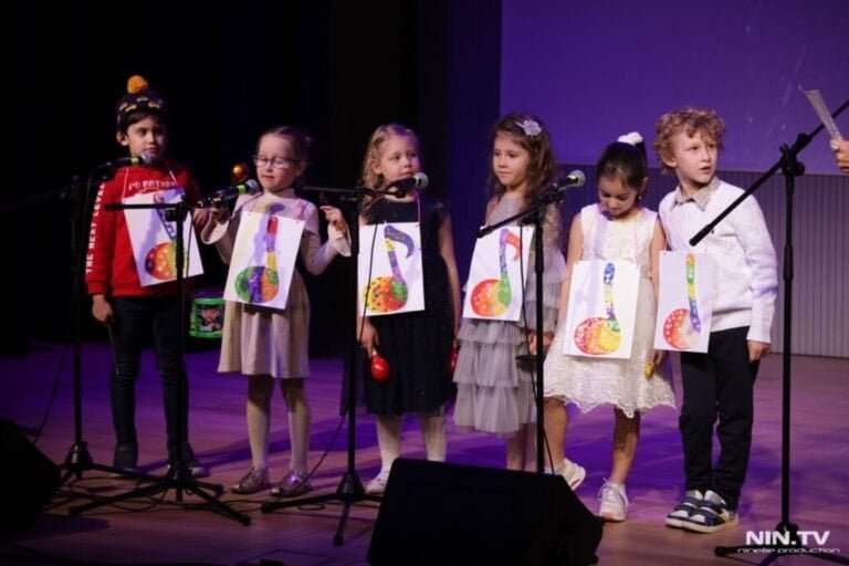 Children on stage with drawings and microphones at a cultural event.
