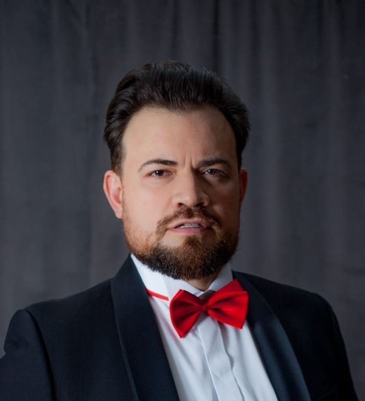 Man with a beard and a red bow tie against a dark background.