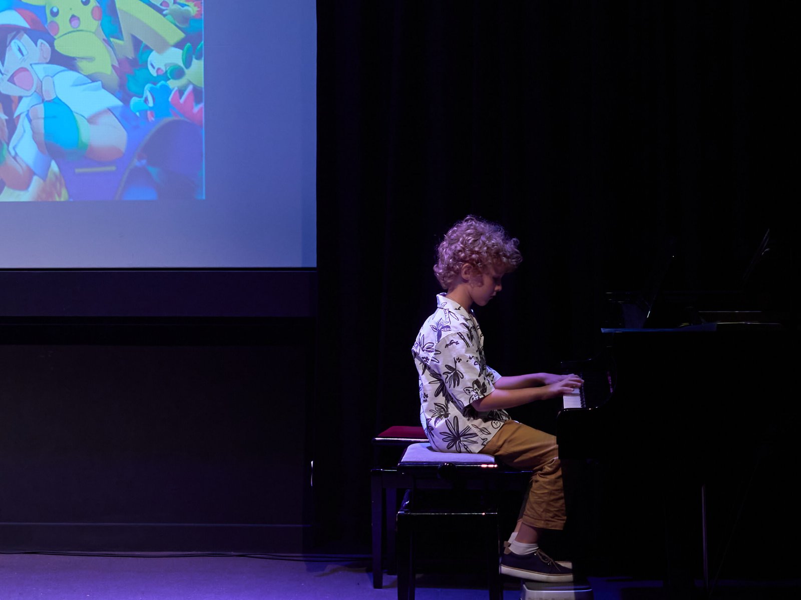 Boy playing the piano on a stage with a projector.