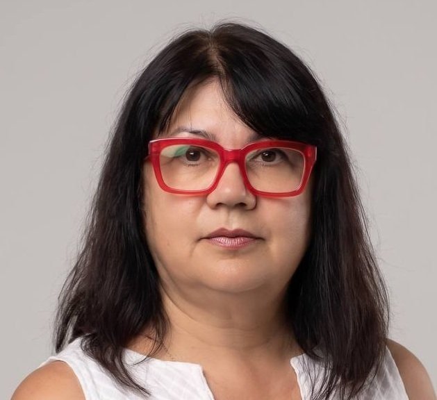 Woman with red glasses and dark hair on a light grey background.