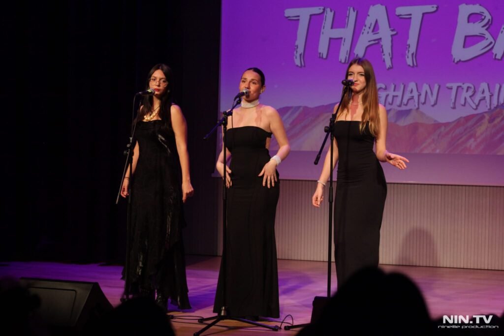 Tres mujeres cantando en un escenario con micrófonos en un evento cultural.