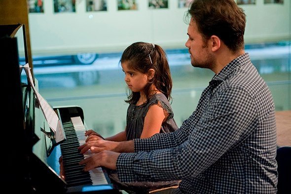 Teacher teaching a girl to play the piano in a cultural centre.