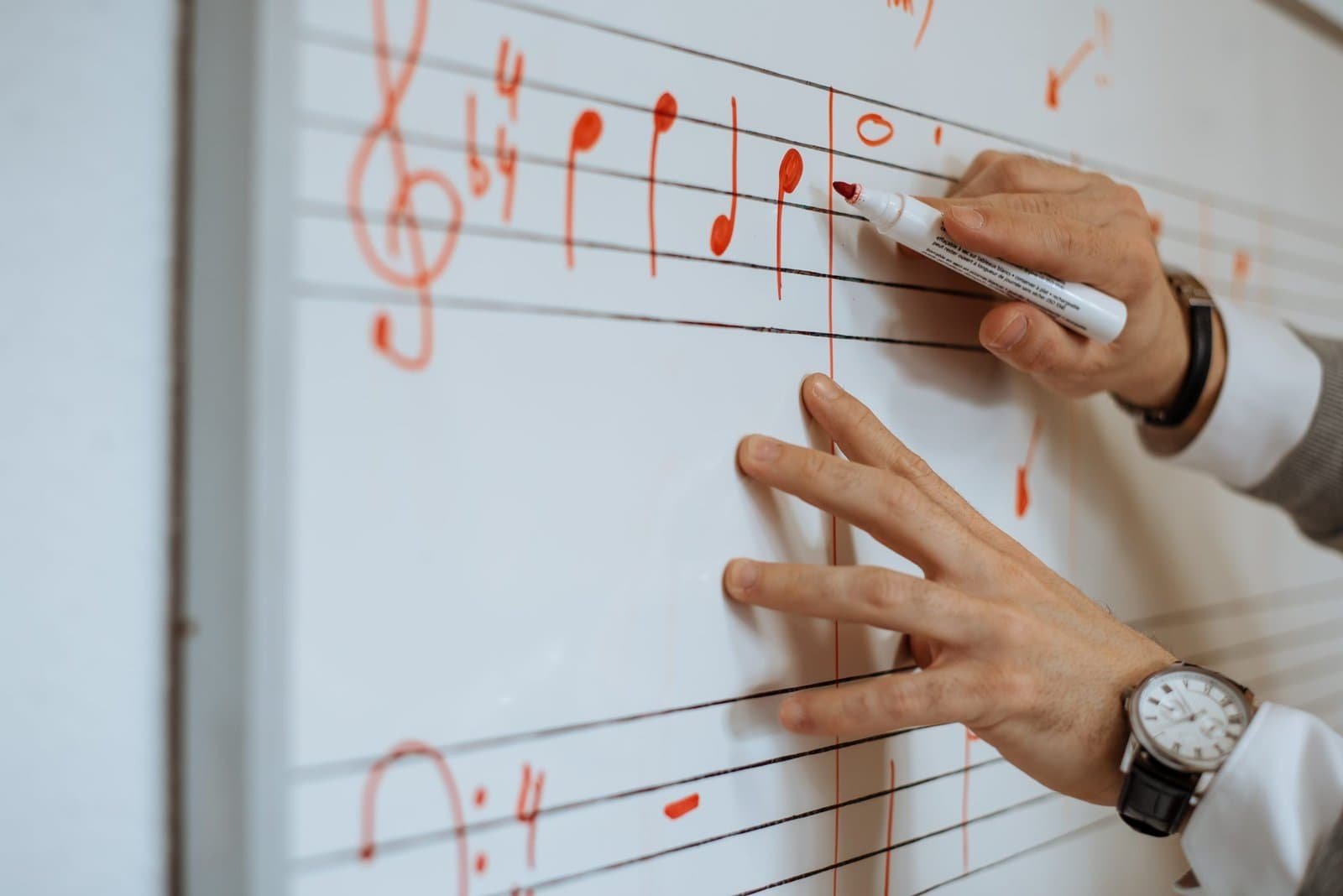 Person writing musical notes on a whiteboard.