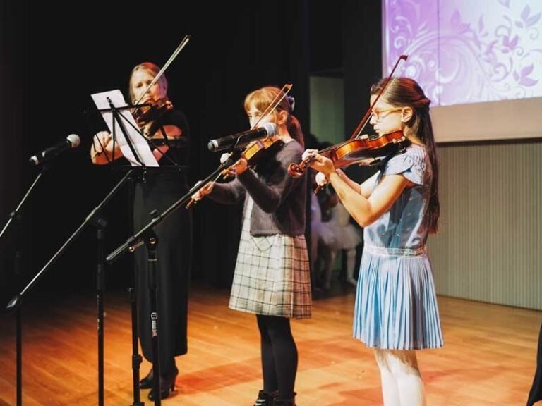 Tres niñas tocando violín en escenario del centro cultural.
