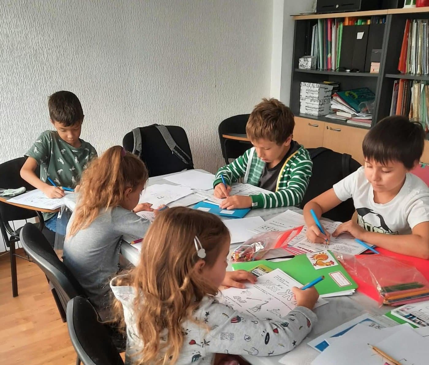 Niños estudiando y dibujando en un aula escolar.